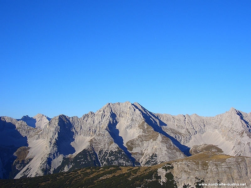 Felsiger Bergkamm mit schroffen grauen Gipfeln unter klarem blauem Himmel, Blick von einem Hügel aus